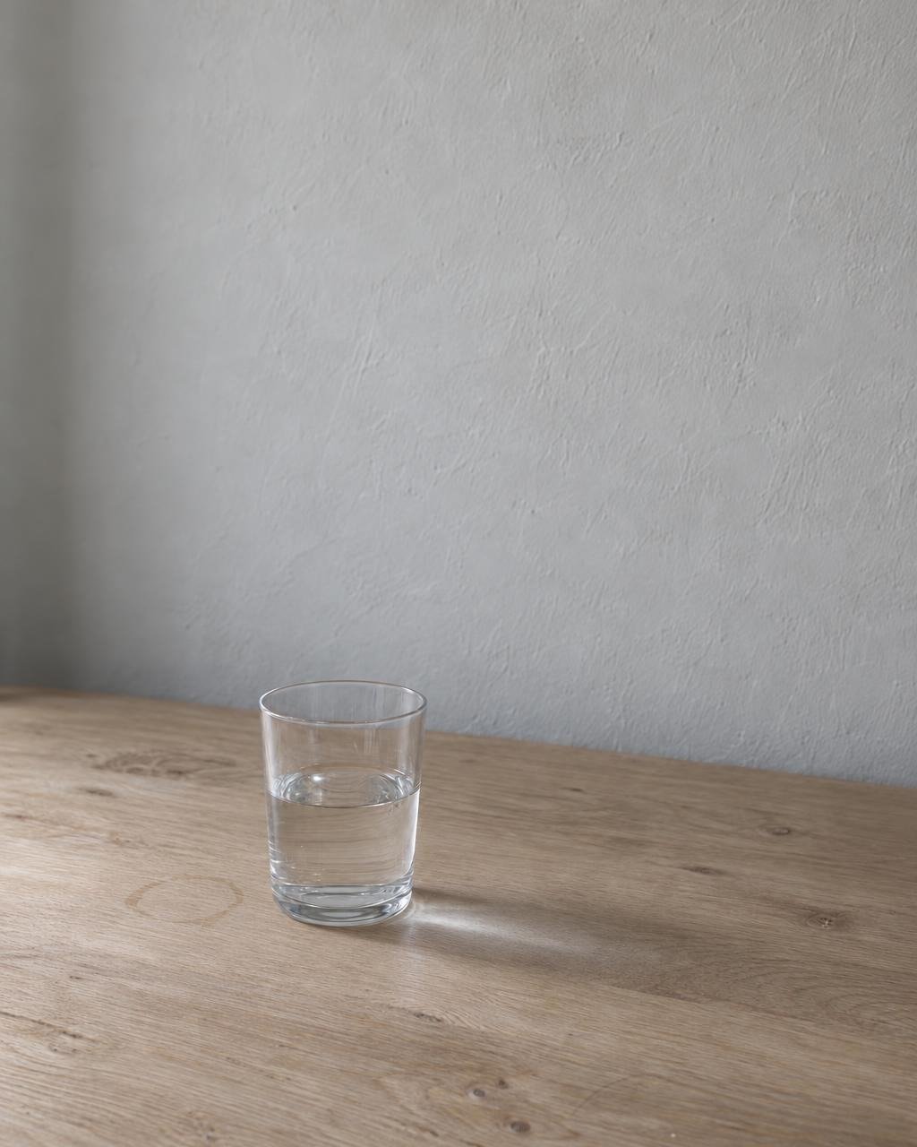 Illustration: a glass of water, half drunk, on a pale oak table in even morning light, a faint water ring beside it.